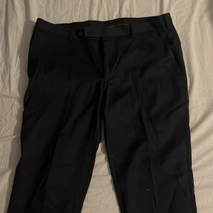 Svarta kostymbyxor - Snygga svarta kostymbyxor med en klassisk design. Byxorna har en rak passform och är perfekta för formella tillfällen. De har knappar och dragkedja framtill samt hällor för bälte.