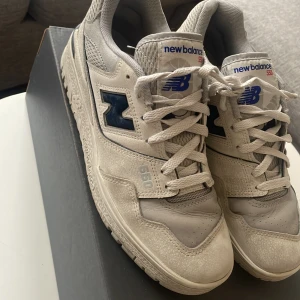 New Balance 550 sneakers - Snygga New Balance 550 sneakers i en stilren vit och grå färgkombination med mörkblå detaljer. Skorna har en klassisk snörning och rund tå, perfekt för en casual look. New Balance-loggan syns tydligt på sidan och hälen. Boxen tillkommer.