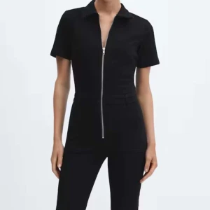 Svart jumpsuit med dragkedja - Svart jumpsuit med kort ärm och hel dragkedja framtill. Den har krage och boutcut, två fickor framtill och markerad midja. Jättefint skick! 