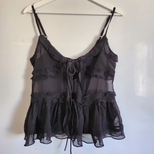 Svart volangtop från ONLY - Säljer en svart, transparent volangtopp från ONLY med smala axelband och knytning fram. Aldrig använd, prislapp kvar. Nypris 249 kr. 