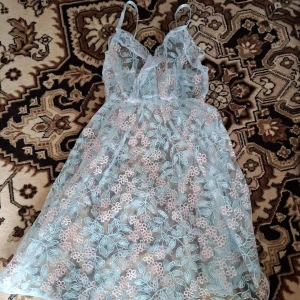 Blommig spetsklänning med tunna axelband - Säljer en ljusblå transparent klänning med blommigt spetsmönster och tunna axelband. Klänningen har en romantisk känsla med vackra broderade detaljer och är perfekt för sommarens varma dagar.