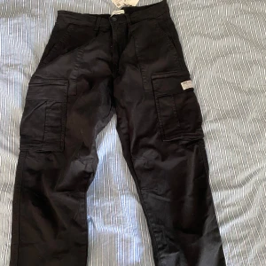 Svarta cargobyxor från Zara - Säljer ett par svarta cargobyxor från Zara med flera stora fickor på benen och klassisk cargomodell. Byxorna har normal passform och är tillverkade i bomull. Perfekta för en avslappnad och trendig stil.