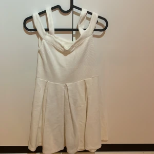 Vit klänning med breda axelband från mint&berry - Söt vit klänning från mint&berry med breda axelband och lätt utställd kjol. Klänningen har en enkel, stilren design och är tillverkad i ett mjukt tyg med diskret struktur. Perfekt för varma dagar eller speciella tillfällen.