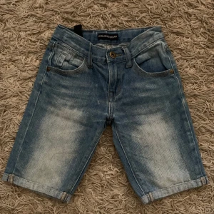 Blå jeansshorts från Dolce & Gabbana - Snygga blå jeansshorts från Dolce & Gabbana med klassisk femficksdesign och uppvikta benslut. Shortsen har slitna detaljer och en normal passform, perfekta för sommardagar.