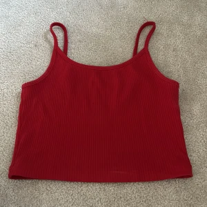 Röd ribbad croppad linnetopp - Säljer en röd croppad linnetopp med smala axelband och ribbad struktur. Perfekt för sommardagar eller att styla lager på lager. Enkel och stilren design som passar till mycket.
