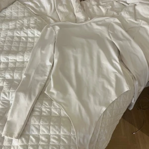 Vit långärmad bodysuit från Bianca x Nelly - Säljer en vit långärmad bodysuit från Bianca x Nelly. Den har en rund halsringning och är tillverkad i ett mjukt, stretchigt material som sitter snyggt på kroppen. Den är knappt använd!