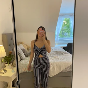 Randig jumpsuit från Hollister - Säljer en snygg randig jumpsuit från Hollister i marinblått och vitt. Jumpsuiten har smala axelband, omlott-topp med v-ringning och en liten cut-out framtill. Byxorna är vida och plagget har en öppen rygg för en cool look.