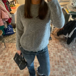 Grå stickad tröja - Mysig grå stickad tröja med rund halsringning och långa ärmar. Perfekt för kyligare dagar och enkel att matcha med jeans eller kjol. Klassisk och stilren design.