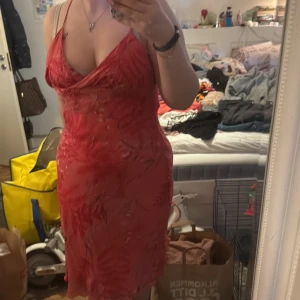 Röd blommig klänning från H&M - Säljer en röd klänning från H&M med blommigt mönster och v-ringning. Klänningen är ärmlös, har en figurnära passform och dragkedja i sidan. Perfekt för sommarens tillfällen!