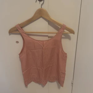 Rosa linnetopp med broderad kant från H&M Divided - Säljer en söt ljusrosa linnetopp från H&M Divided. Toppen är ärmlös och har en broderad kant nertill med blommönster. Perfekt för varma dagar och enkel att matcha med jeans eller kjol.