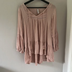 Ljusrosa volangklänning från Amisu - Supersöt ljusrosa klänning från Amisu med volangdetaljer och v-ringning. Klänningen har långärmade ärmar och fina spetsinslag upptill. Perfekt för vår och sommar, lätt och luftig i materialet.priset är inte hugget i sten