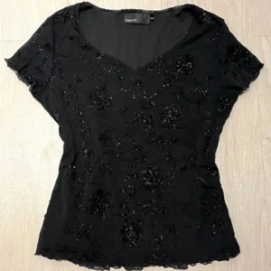 Svart glittrig blus med blommönster - Supersnygg svart blus med glittriga detaljer och blommigt mönster. V-ringad med korta ärmar och lätt transparent tyg. Perfekt för att lyfta vilken outfit som helst med lite extra glitter.