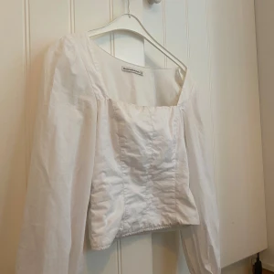 Vit blus med puffärmar från Abercrombie & Fitch - Säljer en vit blus från Abercrombie & Fitch med fyrkantig ringning och långa puffärmar. Toppen har en croppad passform och är tillverkad i ett lätt bomullsmaterial. Perfekt för en trendig och stilren look.