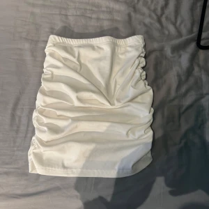 Vit ribbad kjol med rynkade detaljer - Säljer en vit ribbad kjol med snygga rynkade detaljer längs sidorna. Kjolen är kort och har en tight passform.
