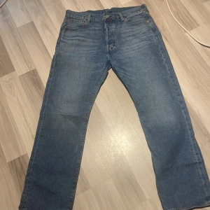 Levi's 501 jeans blå - Klassiska blå Levi's 501 jeans med rak passform. Byxorna har knappgylf och tydlig läderpatch bak i midjan. Perfekta för dig som gillar tidlös denimstil. Varan är även helt oanvänd 