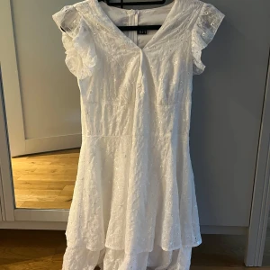 Vit blommig klänning från LoNESS - Superfin vit klänning från LoNESS med broderade blommor och volangdetaljer vid ärmarna. Klänningen har v-ringning, korta volangärmar och dragkedja i ryggen. Perfekt för sommarens alla tillfällen!
