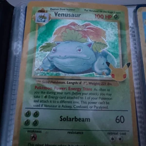 Venusaur Pokémonkort - Säljer ett klassiskt Venusaur Pokémonkort med holografisk yta. Kortet har gröna och gula färger, med en stor växtliknande Pokémon i mitten. Texten är på engelska och kortet har 100 HP. Perfekt för samlare av Pokémonkort. 1995