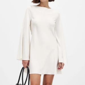 Vit miniklänning i satin med vattenfallsrygg - Stilren vit klänning med långa vida ärmar och en snygg öppen rygg med knytband. Jättefin slutsåld klänning från NA-KD. Helt oanvänd och lappen sitter kvar. Perfekt till student eller skolavslutning!