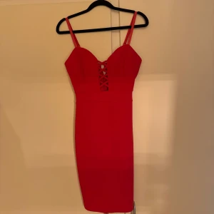 Röd tight klänning med axelband - Säljer en snygg röd tight klänning med smala axelband och dekorativt snörningsmönster framtill. Klänningen är figurnära och slutar ovanför knäna