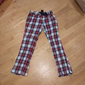 Rutig byxa med rosett från Gina Tricot - Säljer ett par rutiga byxor från Gina Tricot i rött, blått och vitt. Byxorna har en midjeresår med en dekorativ marinblå rosett framtill. Perfekta för en avslappnad stil.