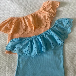 Två one shoulder toppar från Zara - Säljer två one shoulder toppar från Zara i storlek 164. En är ljusblå och en är aprikos, båda med volang längs axeln. Perfekta för sommaren! 250 kr för båda💛