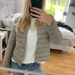 Jacka - Säljer en ljusgrå pufferjacka från Uniqlo. Jackan är lätt vadderad, har knappar framtill och en klassisk, enkel design. Perfekt för övergångsperioder och enkel att matcha med olika outfits.