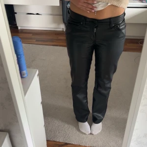 Svarta skinnbyxor med raka ben - Säljer ett par svarta skinnbyxor med normal passform och raka ben. Byxorna har klassisk femficksdesign, dragkedja och knapp framtill. Snygga detaljer och stilren look som passar till många outfits.
