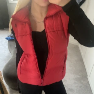 Röd dunväst från Northbrook Sports - Röd dunväst från Northbrook. Västen har två fickor på sidorna och en enkel, sportig design. Perfekt att slänga över en hoodie eller långärmad tröja för extra värme🥰