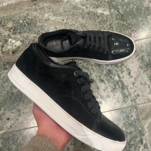 Svarta sneakers från Lanvin med lackad tå - Säljer ett par svarta sneakers från Lanvin med snygg lackad tå och vit sula. Skorna har snörning och en klassisk rund tå. Perfekta för dig som gillar stilrena och exklusiva sneakers. Storlek passar 42 äkta självklart