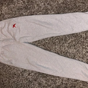 Ljusgrå mjukisbyxor från Axel Arigato - Snygga ljusgrå mjukisbyxor från Axel Arigato med röd broderad logga på höften. Byxorna har resår i midjan och är perfekta för en avslappnad stil. Mjukt material och klassisk passform.