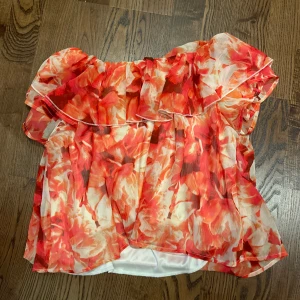 Blommig offshoulder blus - Säljer en blommig offshoulder blus i rött,ä och vitt. Toppen har volang upptill och är luftig med en croppad passform. Perfekt för varma dagar och ger en somrig känsla. Den är väldigt stretchig och passar XS till M