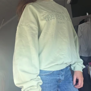 Grön sweatshirt med tryck - Säljer en grön sweatshirt med tryck på framsidan. Tröjan har långa ärmar och en avslappnad passform, perfekt för en casual look. Den är gjord i ett mjukt material som känns skönt mot huden.