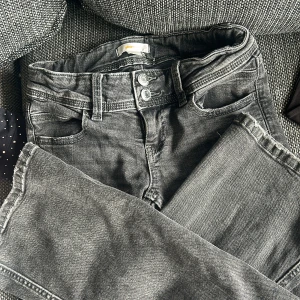 Svarta/grå jeansbyxor från Gina Tricot - Svarta(grå) jeansbyxor från Gina Tricot med dubbla silverfärgade knappar i midjan och klassiska fem fickor. Jeansen har en något tvättad look och bootcut. Perfekta för en avslappnad stil.