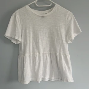 Vit blus med volang - Säljer en söt vit blus med korta ärmar och volang nedtill. Perfekt för en enkel och stilren look. Blusen har rund halsringning och är tillverkad i ett mjukt material. I storlek S men passar bättre xs skulle jag säga. 