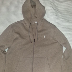 Ralph Lauren hoodie  - Hoodie från Ralph Lauren med dragkedja och justerbar huva. Tröjan har en broderad logotyp på bröstet och praktiska fickor framtill.