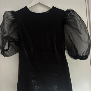 Svart topp med puffärmar - Säljer en svart tröja med stora, transparenta puffärmar. tröjan har en rak passform och rund halsringning. Perfekt för dig som vill sticka ut med en trendig och elegant look.