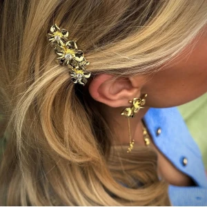 Guld hårspänne med blommor - Elegant guld hårspänne dekorerat med blommor. Perfekt för att ge en extra touch till din frisyr. Blommorna har en glittrig detalj i mitten som fångar ljuset vackert. Helt ny med prislappen kvar 