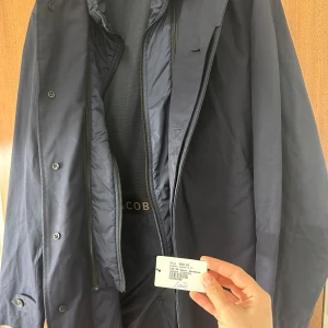 Mörkblå rock från Oscar Jacobson - Elegant mörkblå rock från Oscar Jacobson  med knappar framtill och en stilren design. Rocken har långa ärmar och en klassisk krage, perfekt för en sofistikerad look.