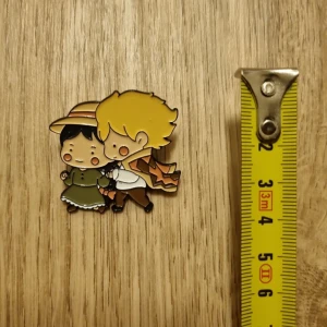 Söt emaljpin med parmotiv, ghibli, levande slottet - Charmig emaljpin föreställande ett par i vintagekläder från ghiblis det levande slottet. Perfekt som accessoar för att ge en personlig touch till din outfit. Paret är klädda i grönt och brunt med detaljer som hatt och kappa.