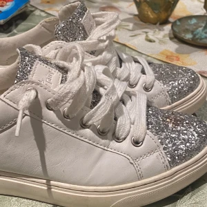 Vita sneakers  - Säljer ett par vita sneakers från Jenny Fairy med glittriga silverdetaljer på tån och plösen. Skorna har vita snören och en rund tå. Jättesnygga, men är tyvärr för små för mig. Dem har inga större defekter. 