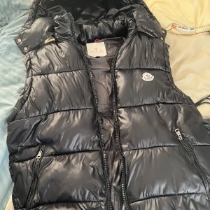 Svart dunväst från Moncler - Säljer en svart dunväst från Moncler med klassisk quiltad design och dragkedja framtill. Västen har två fickor med dragkedja och Moncler-logga på bröstet. Perfekt för lager-på-lager och stilren look. jag har S-M och den sitter perfekt på mig så skulle rekommendera runt M