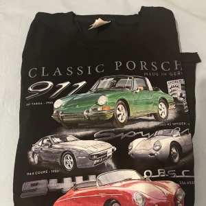 Black t shirt with porches and other cars - Cool svart t-shirt med tryck av klassiska Porsche-bilar i olika färger och modeller. T-shirten har rund hals och korta ärmar. Perfekt för dig som gillar bilar och retrostil.