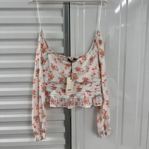 Blommig blus med volang från Bik Bok - Supersöt blommig blus från Bik Bok i vitt med rosa och orange blommor. Långärmad modell med volang nertill och lätt rynkade detaljer. Perfekt för vår och sommar!