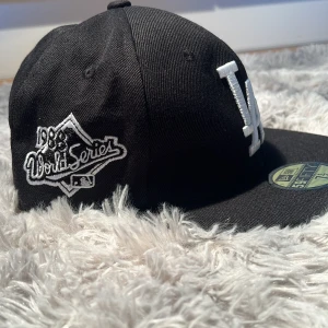 Svart keps från New Era 59FIFTY LA Dodgers - Väldigt unik keps med LA Dodgers-logga framtill och 1988 World Series broderad på sidan. Kepsen har platt skärm och klassisk passform. Undersidan av skärmen är grå med MLB-hologram. Helt ny helt och oanvänd 