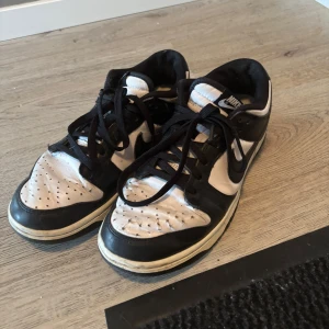 Nike Dunk Low svartvita sneakers - Svartvita Nike Dunk Low sneakers med klassisk design och svart swoosh på sidan. Skorna har snörning och rund tå, samt vit sula. Perfekta för dig som gillar streetwear och vill ha en ikonisk look.