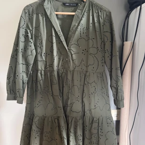 Grön klänning med broderade detaljer från Zara - Säljer en vacker grön klänning från Zara med broderade blommönster och trekvartsärmar. Klänningen har en luftig passform och en v-ringad hals. Perfekt för vår och sommar!