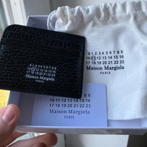 Plånbok Maison Margiela - Säljer en stilren cardholder från Maison Margiela. Kortfodralet har en elegant präglad yta och flera fack för kort. Perfekt för att hålla dina kort organiserade med stil. Inga som helst defekter hör av dig vid minsta fråga!