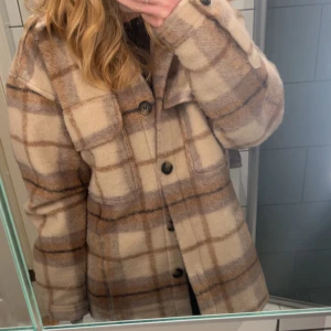 Beige Vår/höstjacka - Säljer en snygg beige och brun rutig jacka med knappar. Jackan är lite oversized men passar ungefär som en medium. Passar perfekt till höst och vår. Använd fåtal gånger