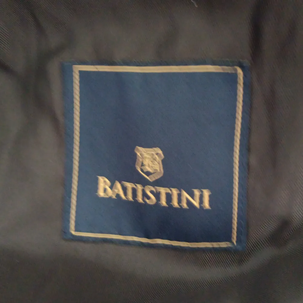 Snygg svart trenchcoat från Batistini med dubbelknäppning och klassisk krage. Jackan har långa ärmar och justerbara remmar vid ärmsluten för en stilren look. Perfekt för höst och vår!. Takit.
