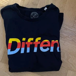Diffen tröja - Säljer en svart t-shirt från Djurgården med ett stort, färgglatt 'Diffen' tryck i gult, rött och blått på framsidan. Perfekt för alla Djurgården-fans! 💛❤️💙lite slitet vid trycket